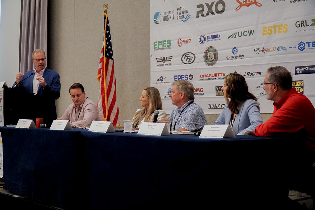 Panelists engaged in a discussion about the Western NC warehouse industry at a logistics conference, with an audience and sponsors in the background.